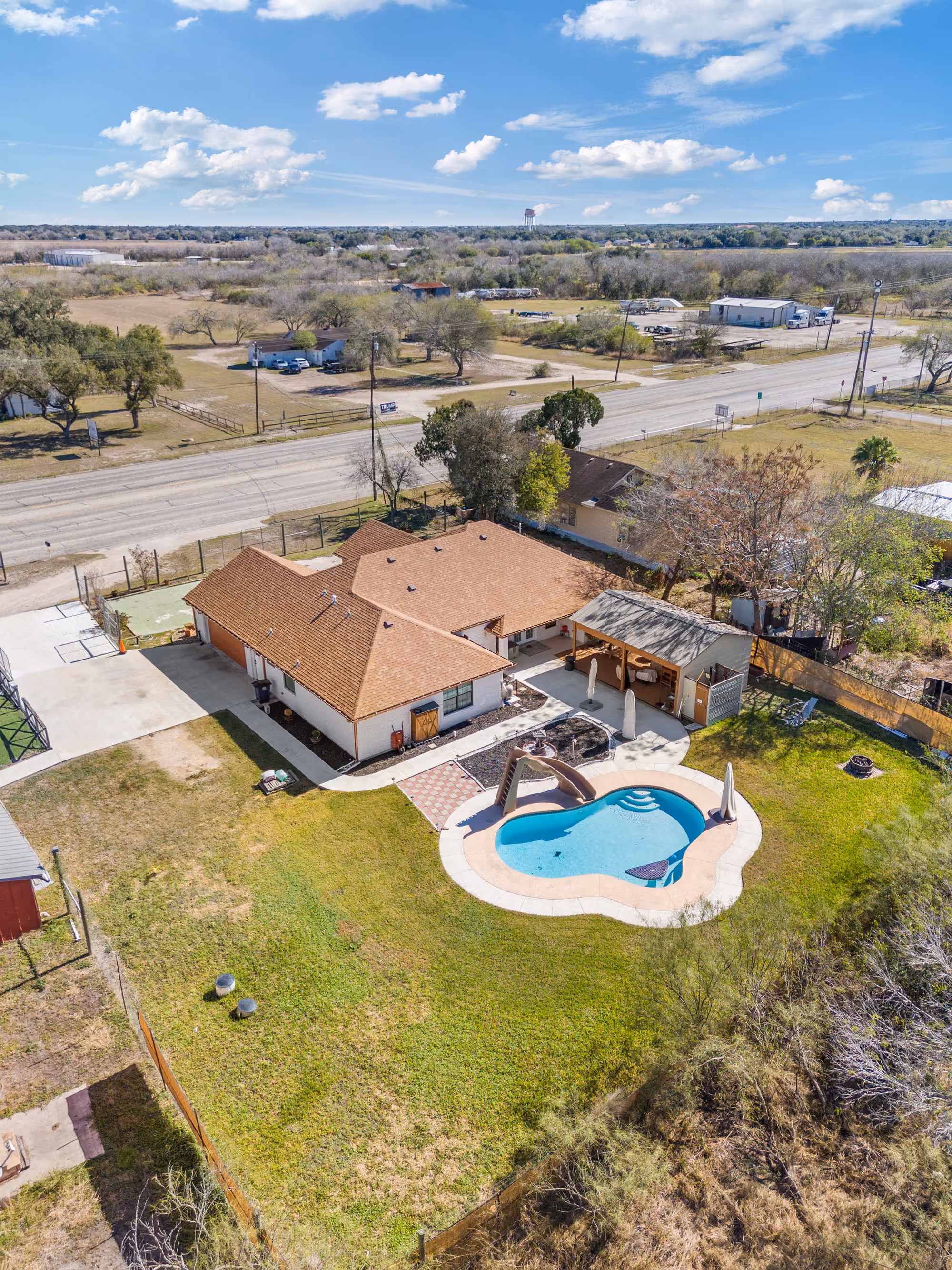 Aerial of the white brick home with its freeform pool and rear patio