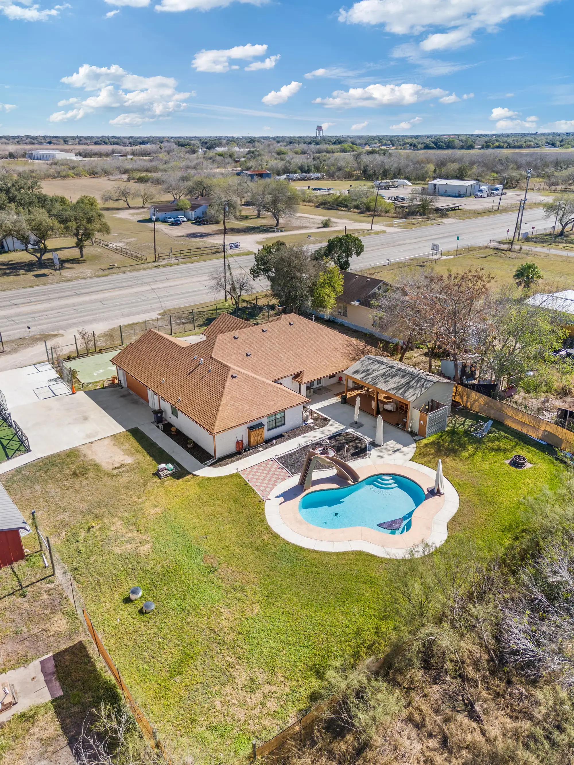 Aerial of the white brick home with its freeform pool and rear patio