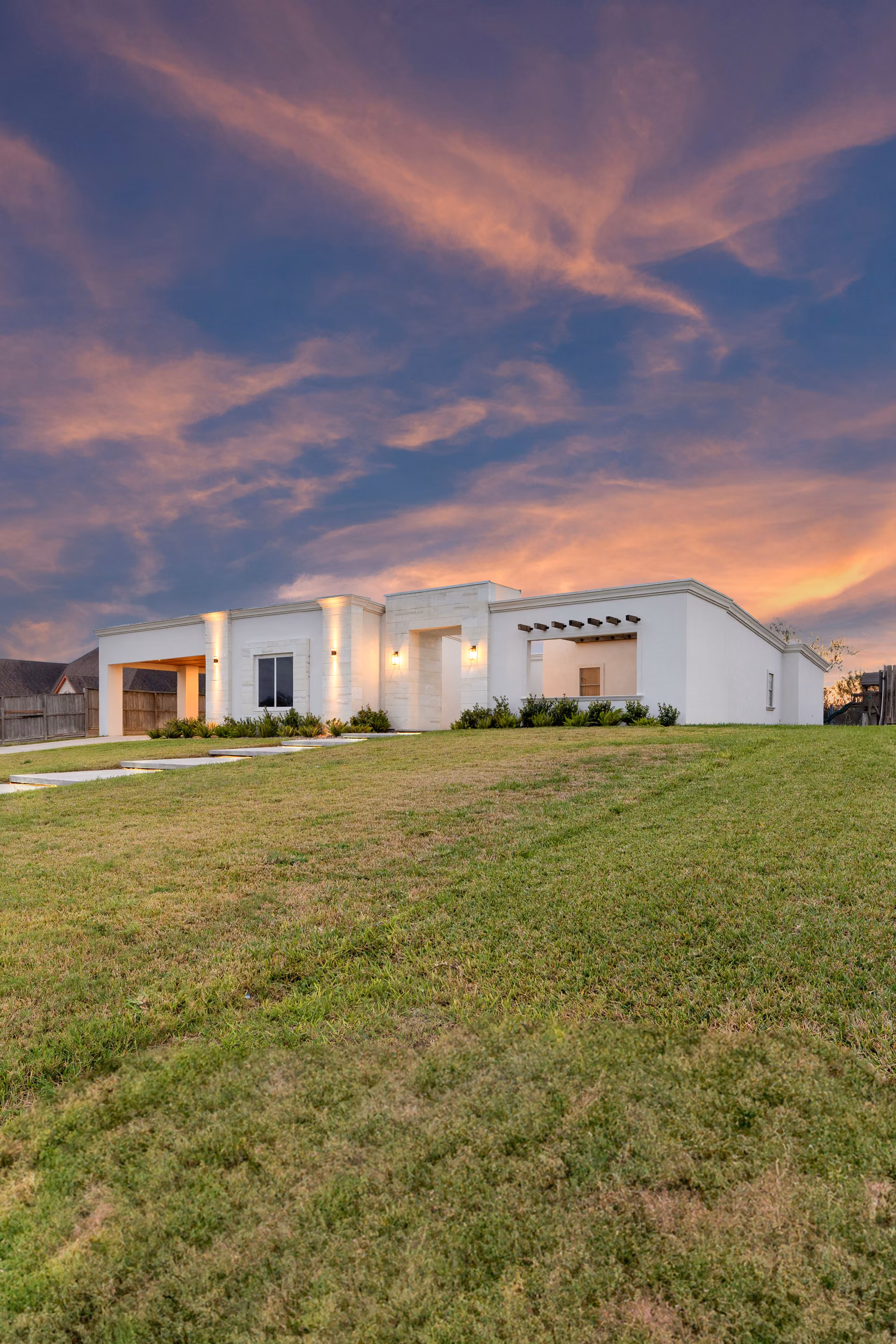 Contemporary white stucco elevation at dusk, coral sky above a flat parapet roofline
