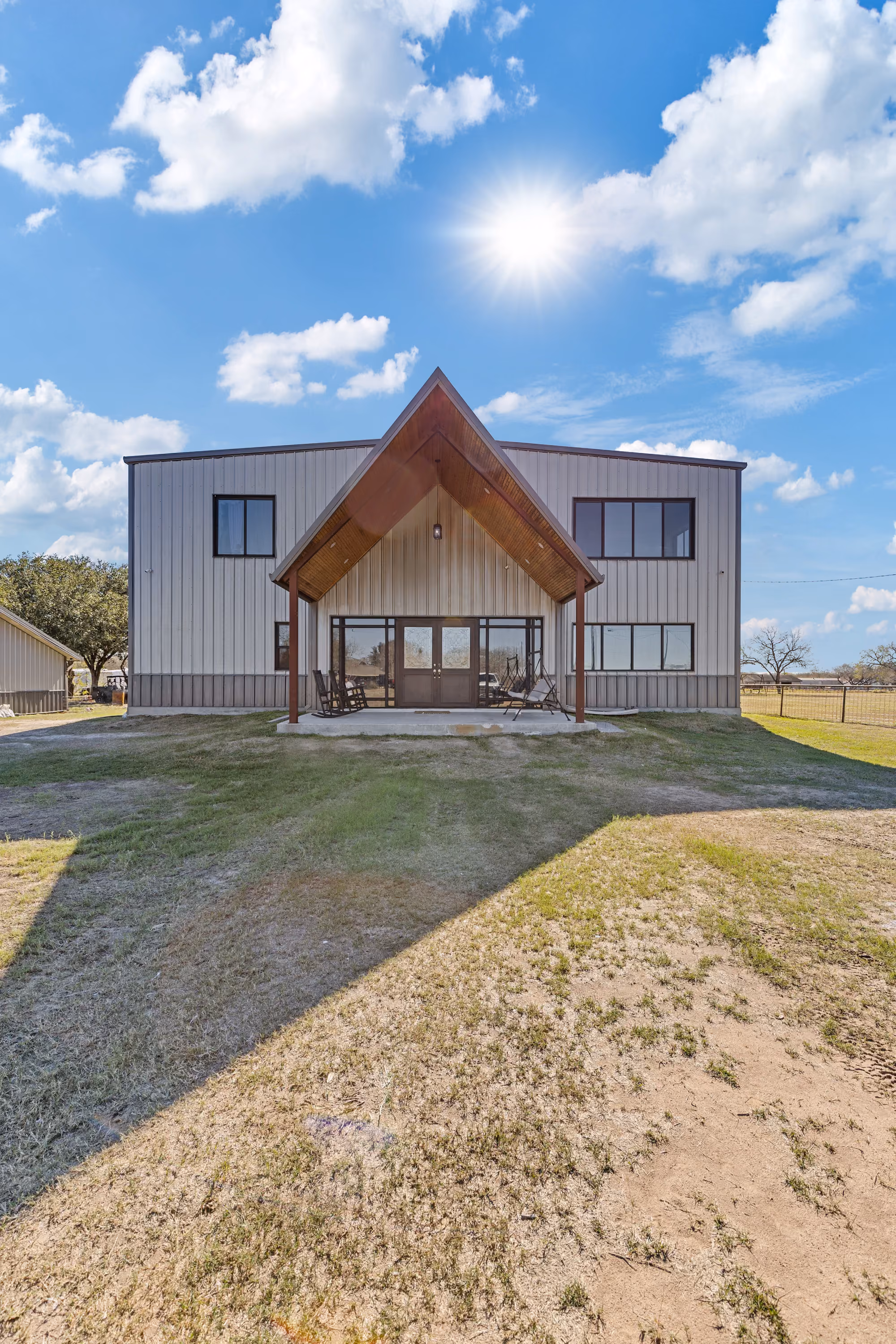 Two-story barndominium with a wood-clad central gable porch in full sun