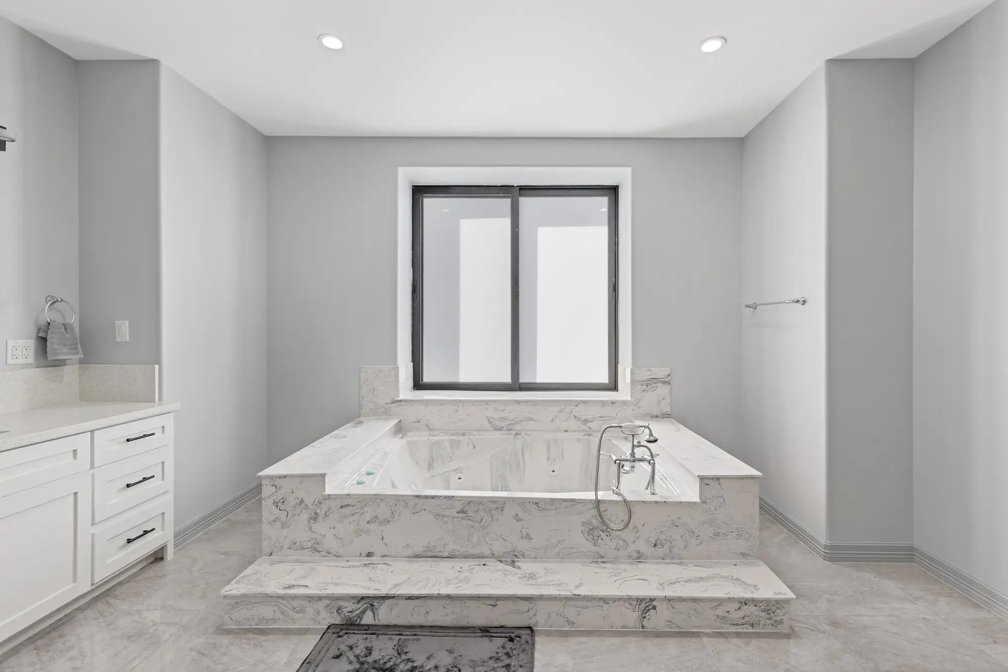 Primary bath with a tub on a marble platform beside a slider window