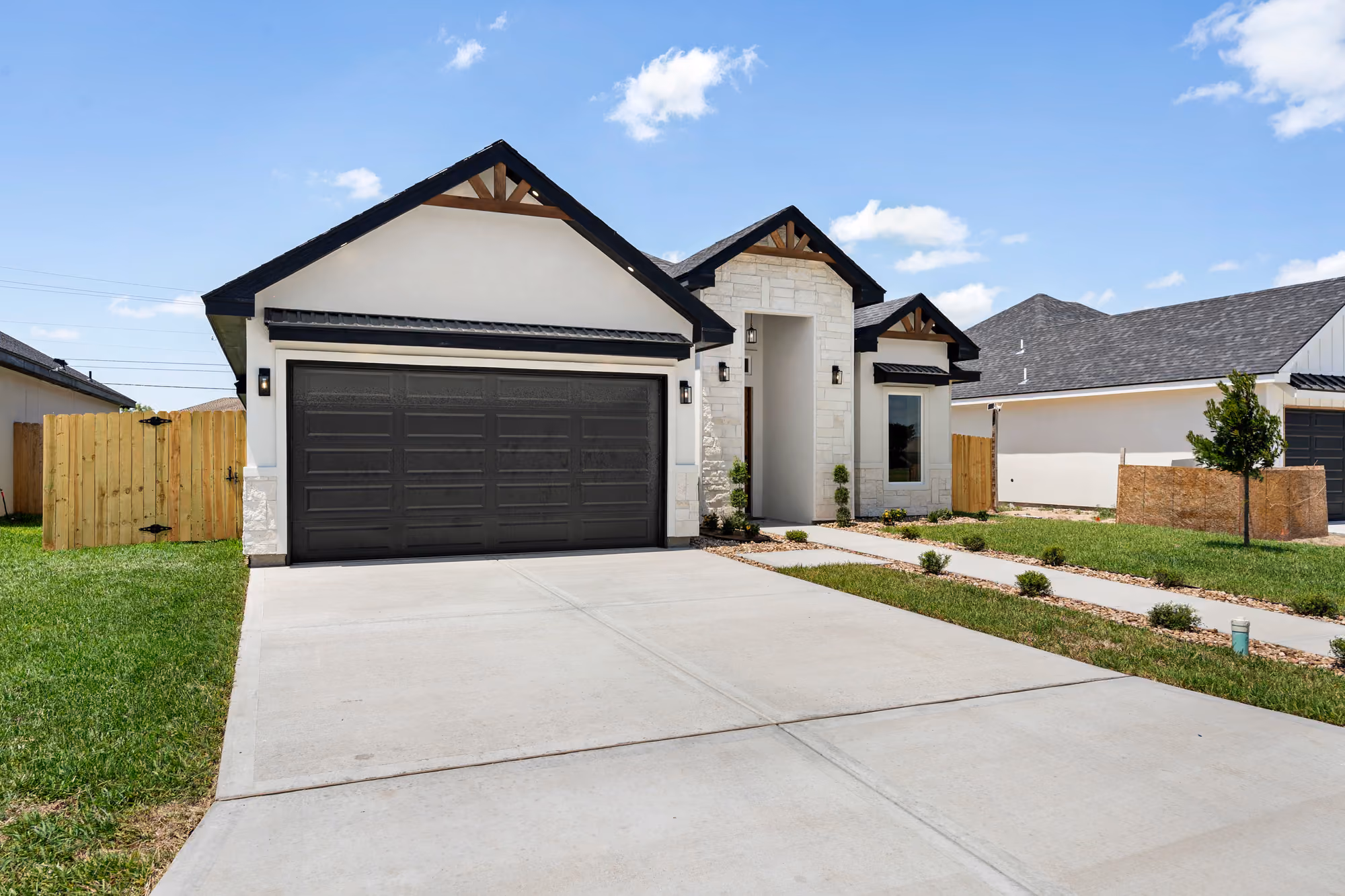 Front elevation in daylight: stone veneer, dark garage door and planted entry bed