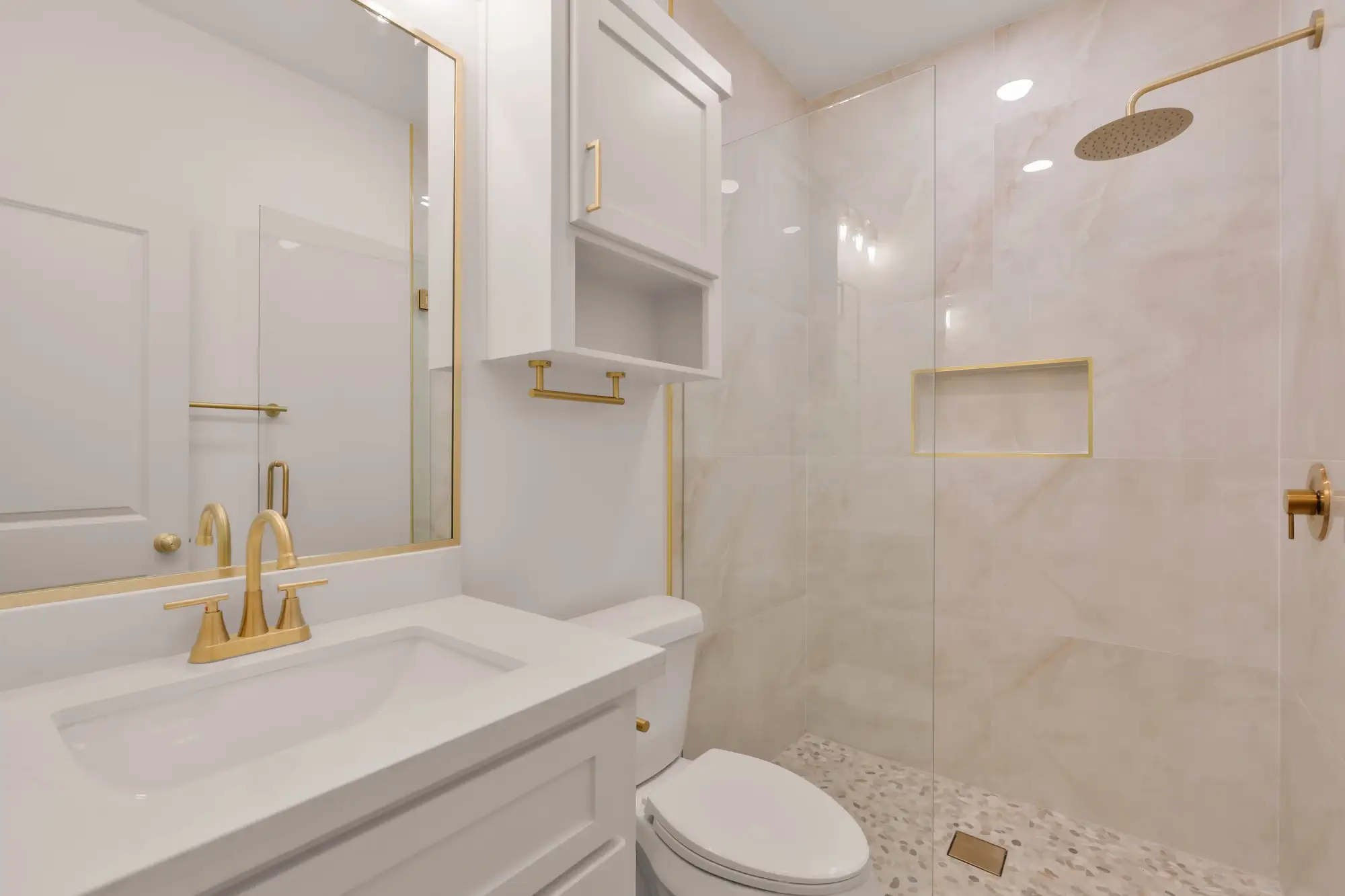 Secondary bath tiled to the ceiling with a brass wall sconce above the mirror
