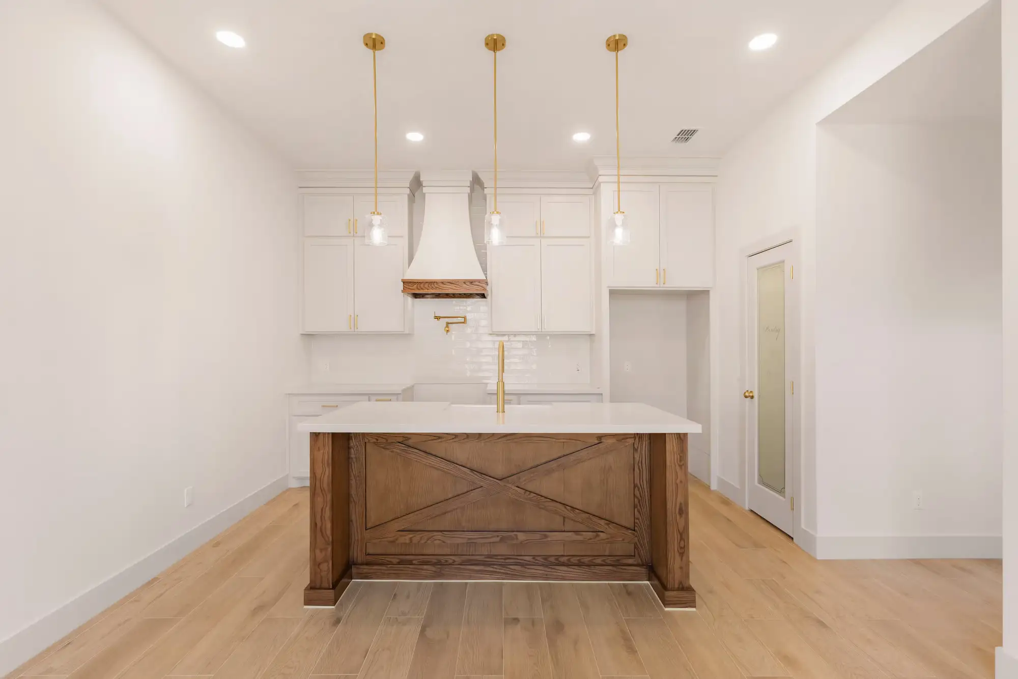 Kitchen island with an X-brace white oak face and wood-wrapped hood under brass pendants