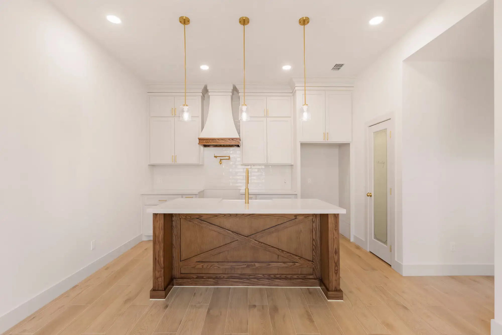 Kitchen island with an X-brace white oak face and wood-wrapped hood under brass pendants