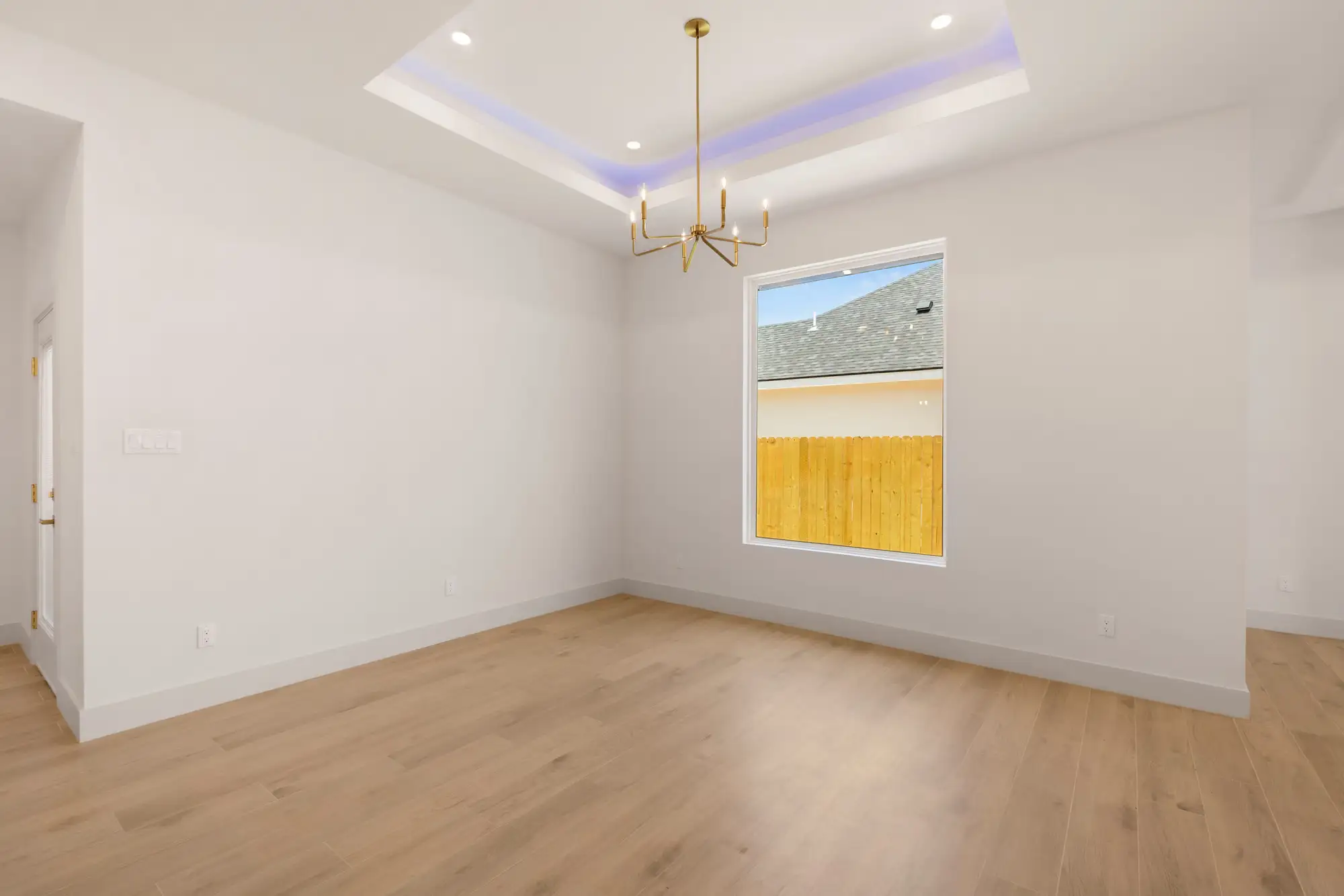 Primary bedroom with a tray ceiling, perimeter cove lighting and a window to the rear lot