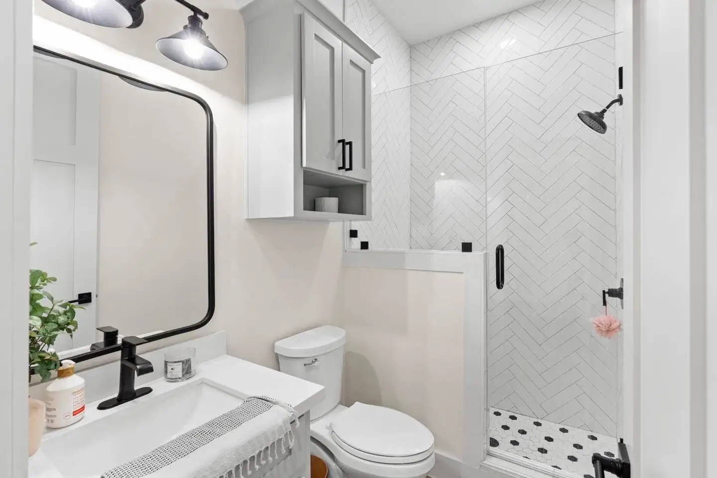 Bath with a black-framed mirror, herringbone tile and matte black fixtures