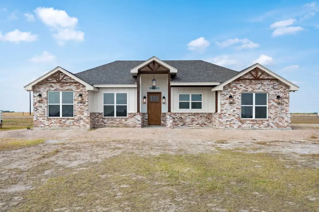 Modern farmhouse elevation with a brick base, timber porch and open acreage around it