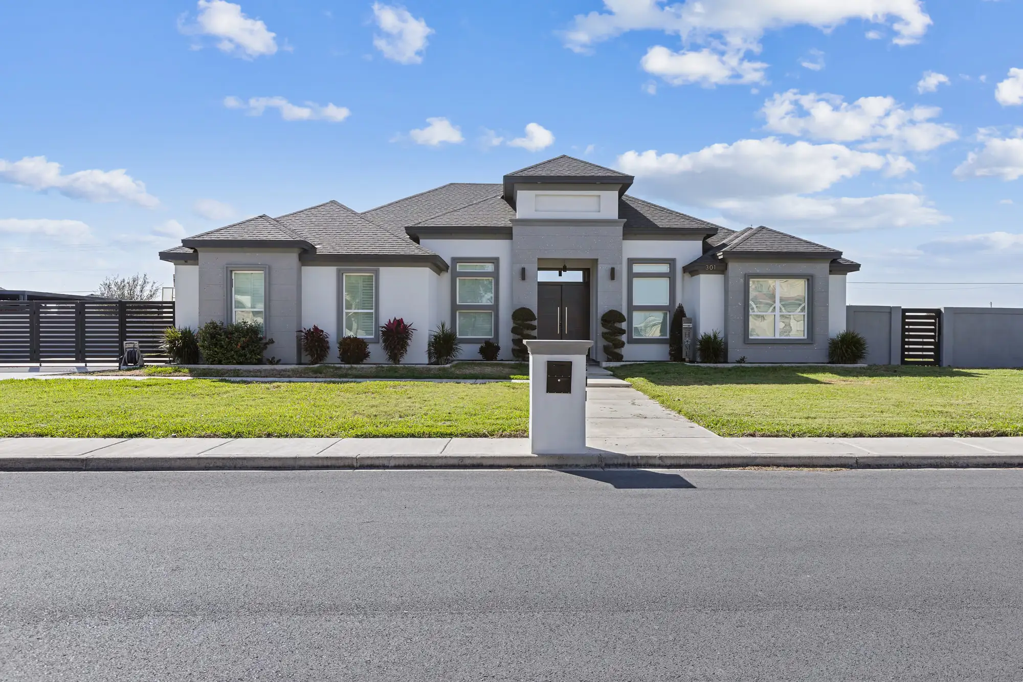 Modern gray-and-white elevation with a low hip roof and newly installed front lawn
