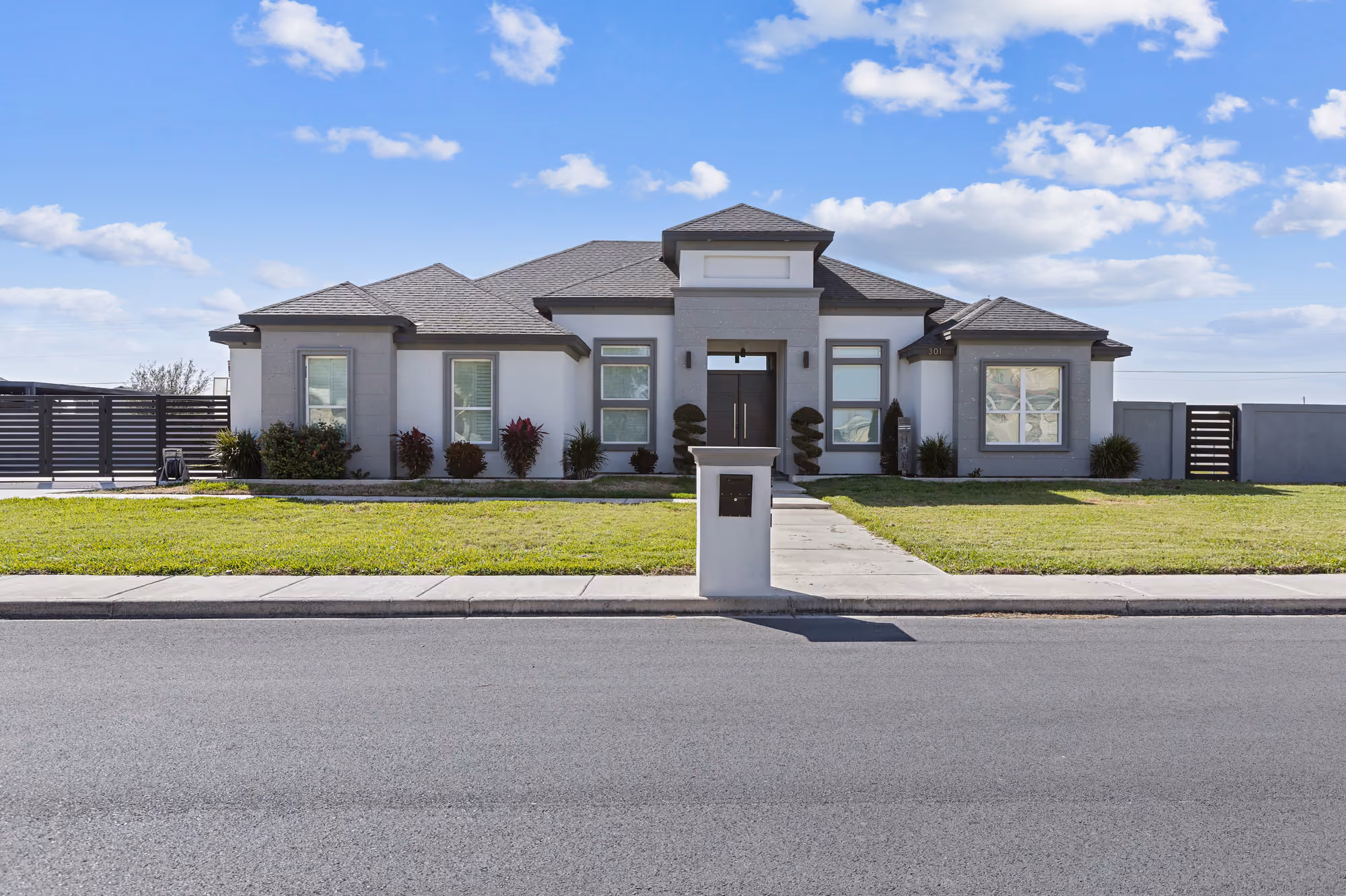 Modern gray-and-white elevation with a low hip roof and newly installed front lawn