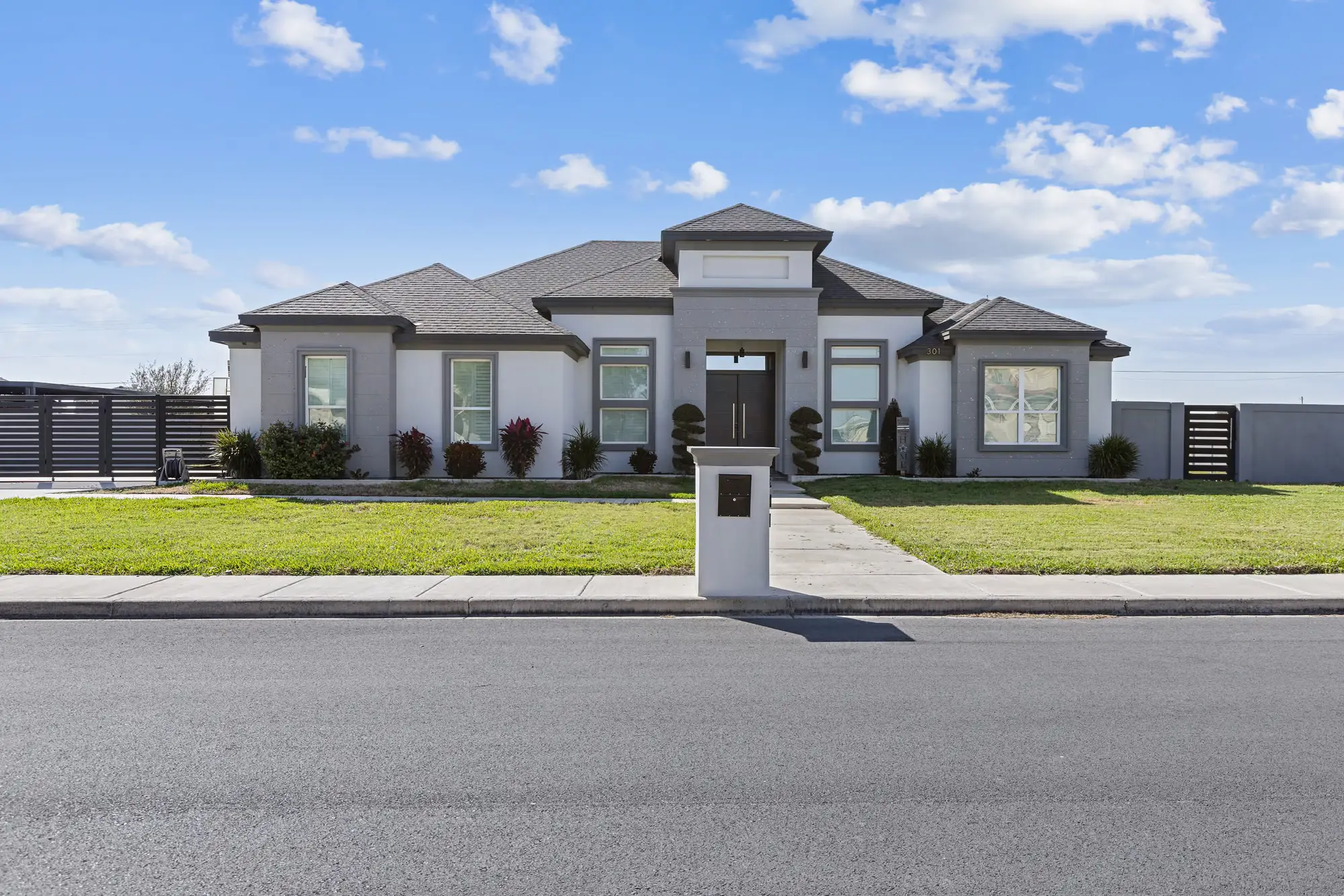Modern gray-and-white elevation with a low hip roof and newly installed front lawn
