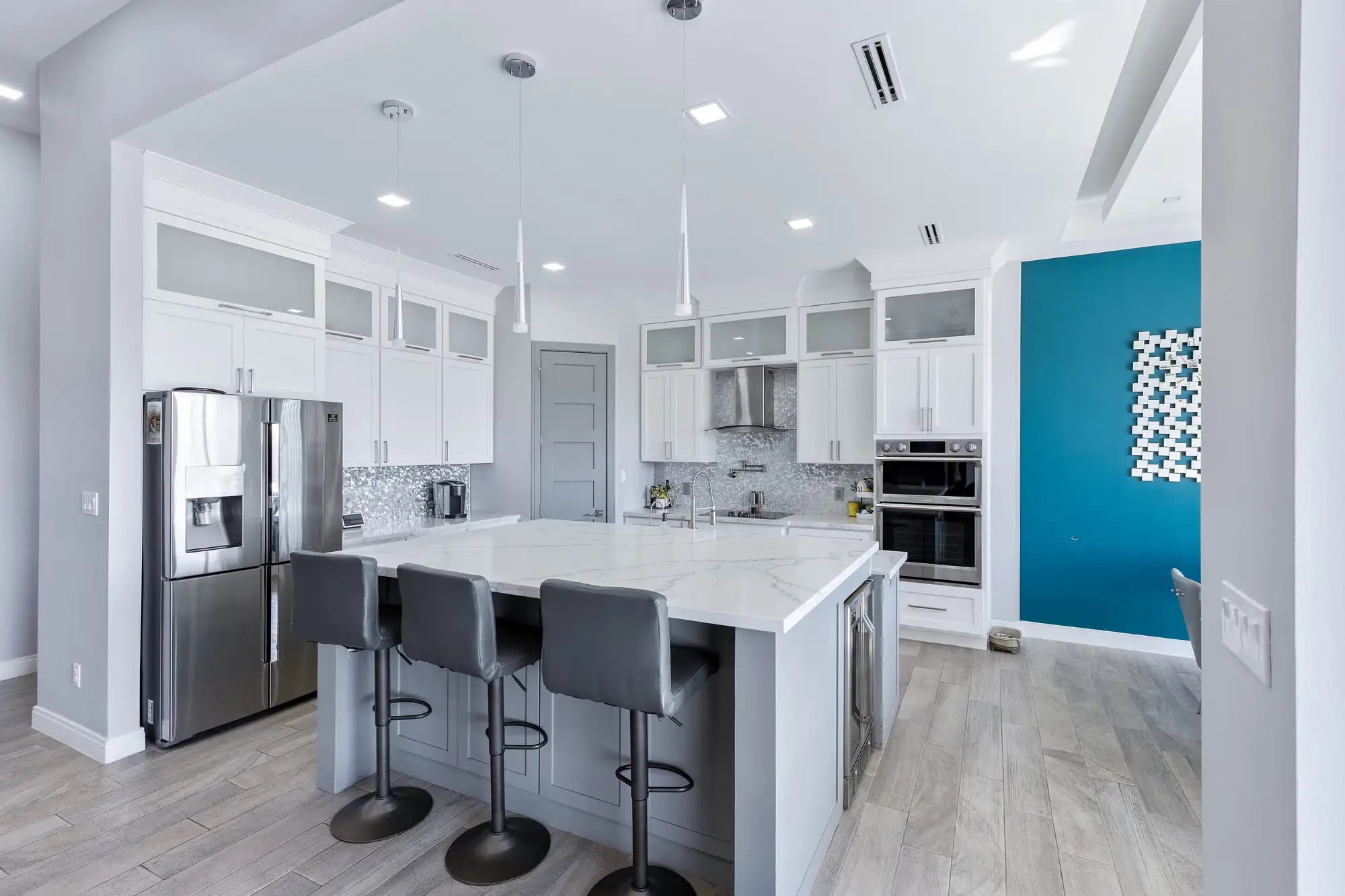 Kitchen island in veined quartz with counter stools and a teal accent wall
