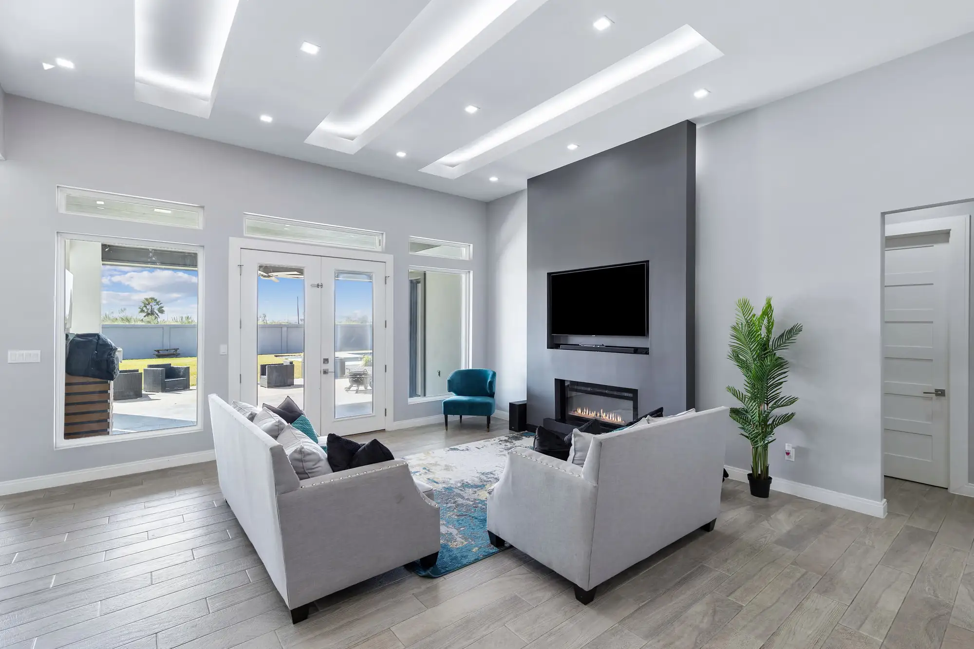 Living room with a lit tray ceiling, recessed fireplace and French doors to the patio