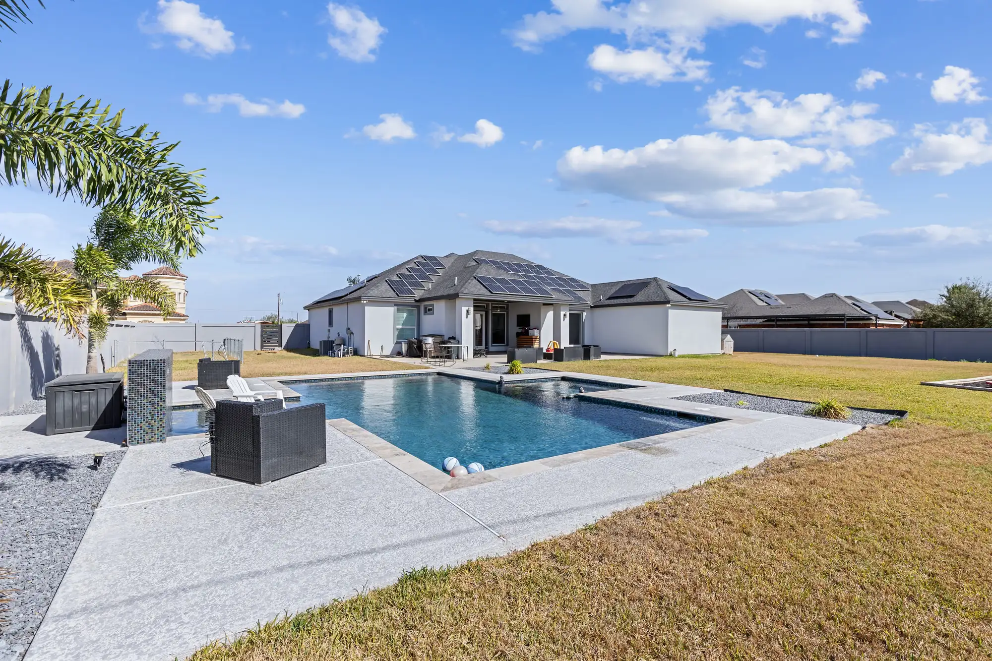 Rectangular pool with an outdoor lounge and palms in the back yard