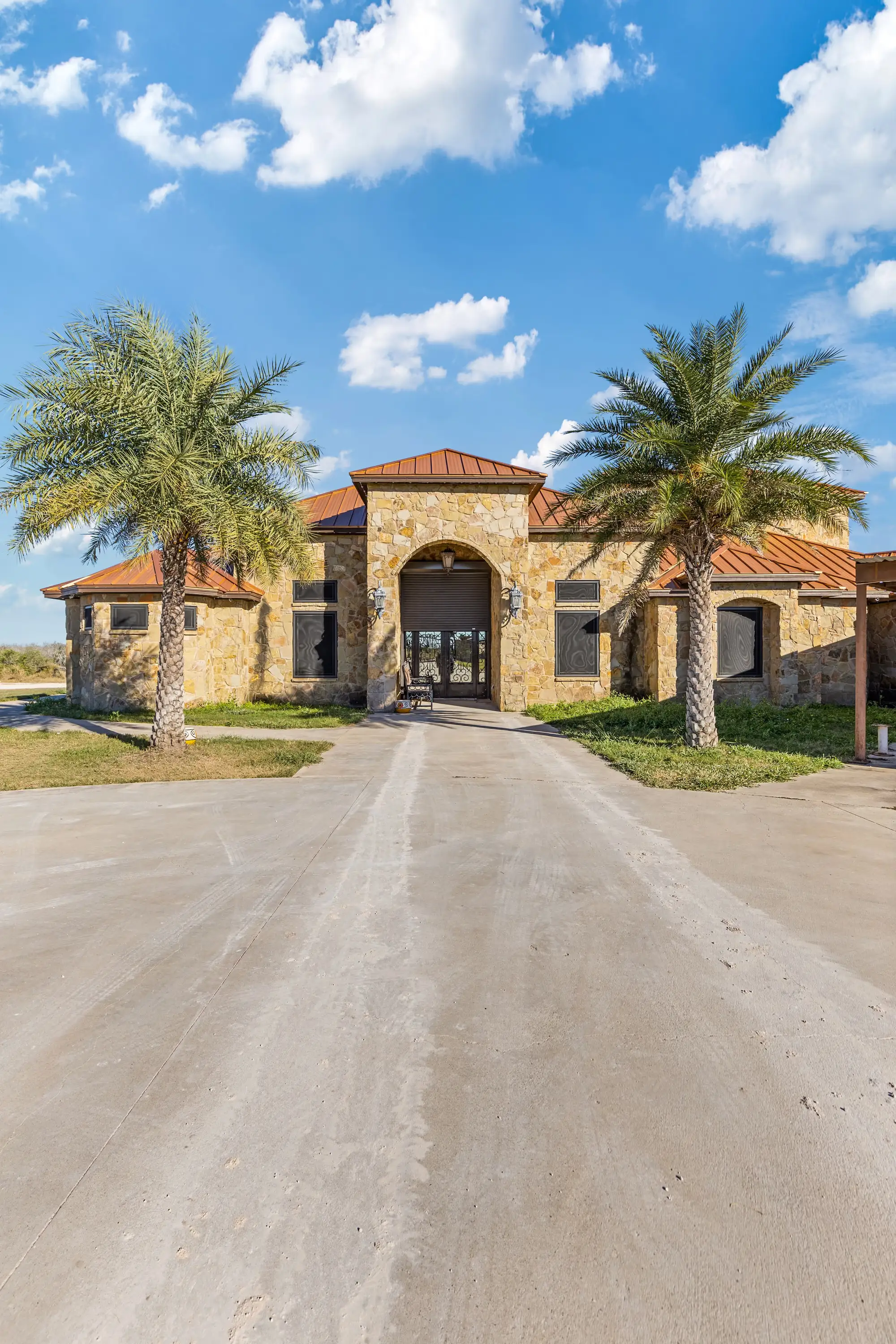 Stone entry arch flanked by palms at the end of the drive