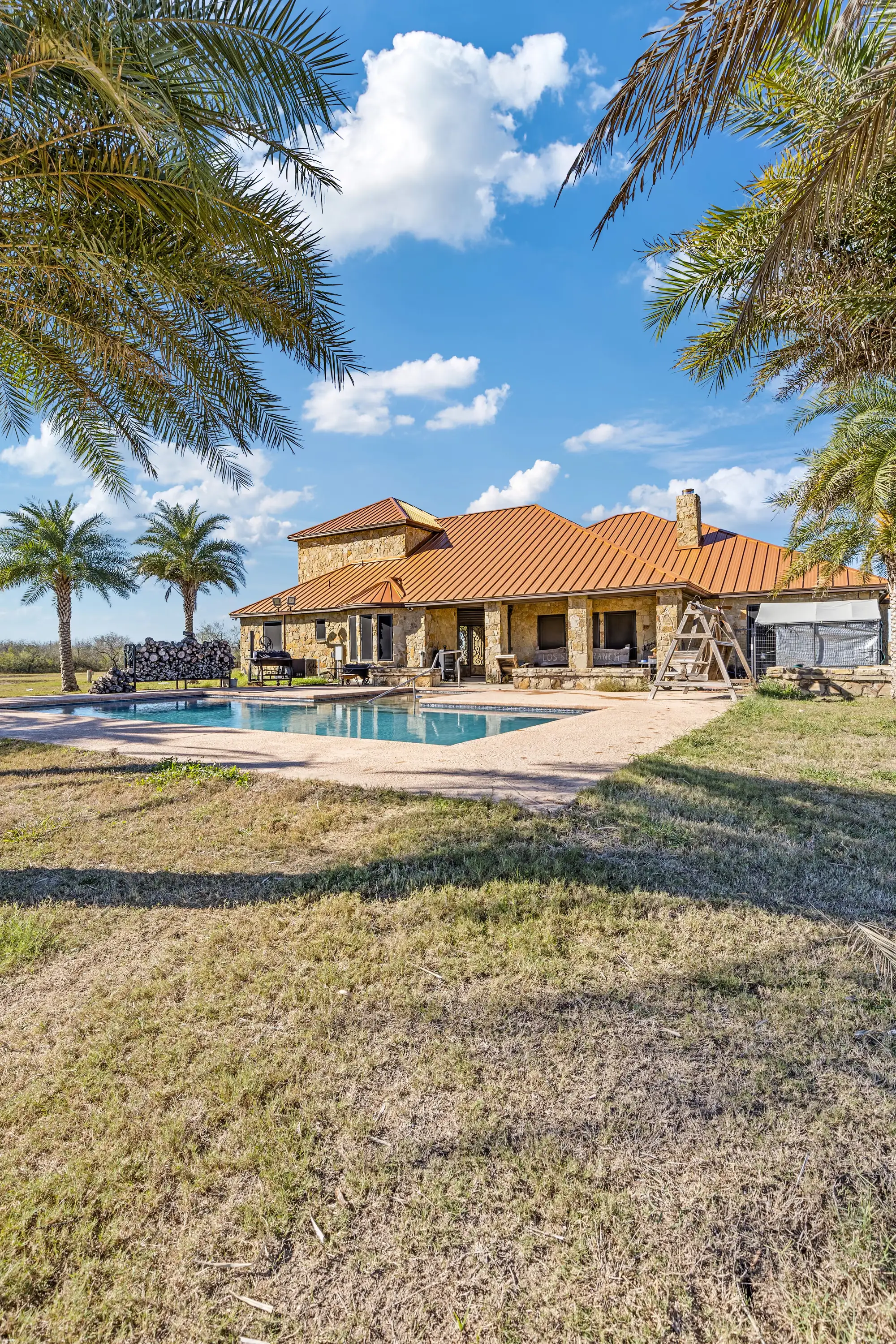 Pool and date palms in front of the stone ranch-style home with its tile roof